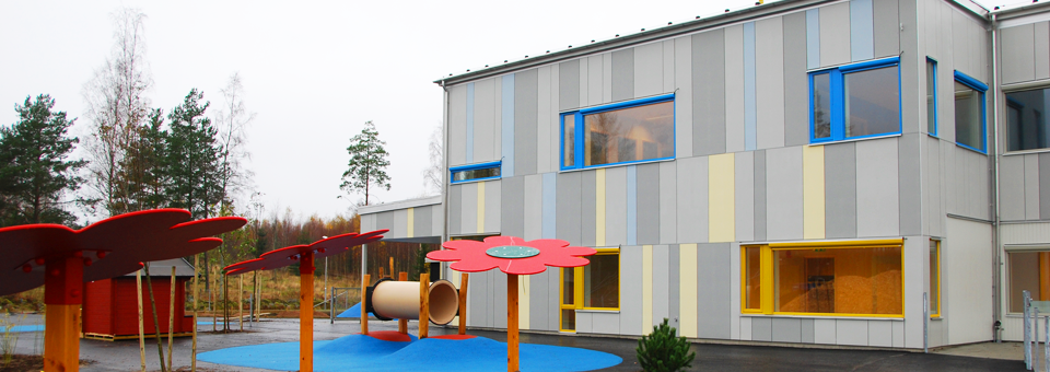 Bild på förskolebyggnad med blåa och gula detaljer och en lekpark i förgrunden.
