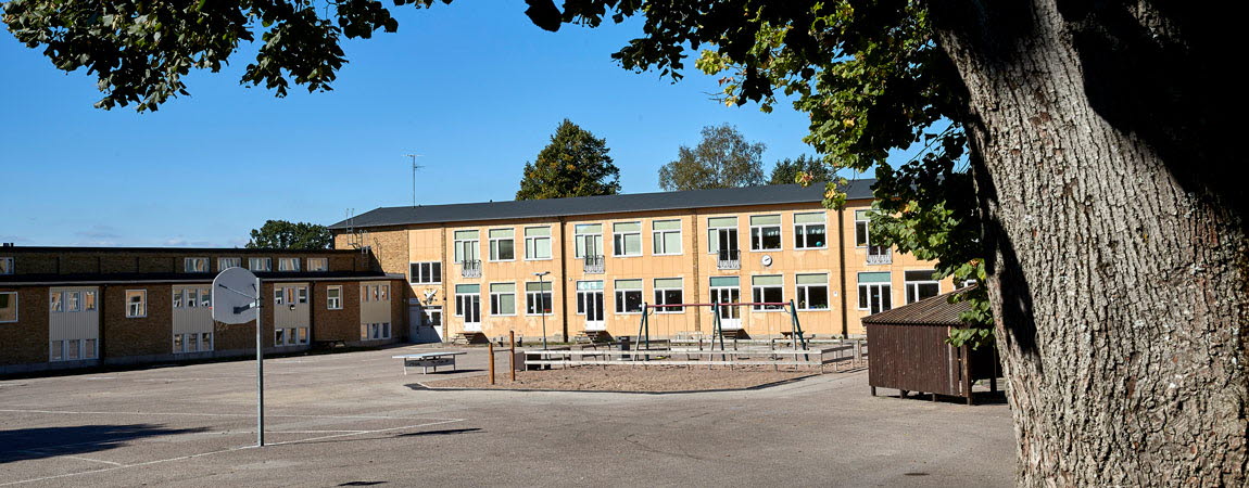 Gul tegelbyggnad, på skolgården står en gungställning och en basketplan