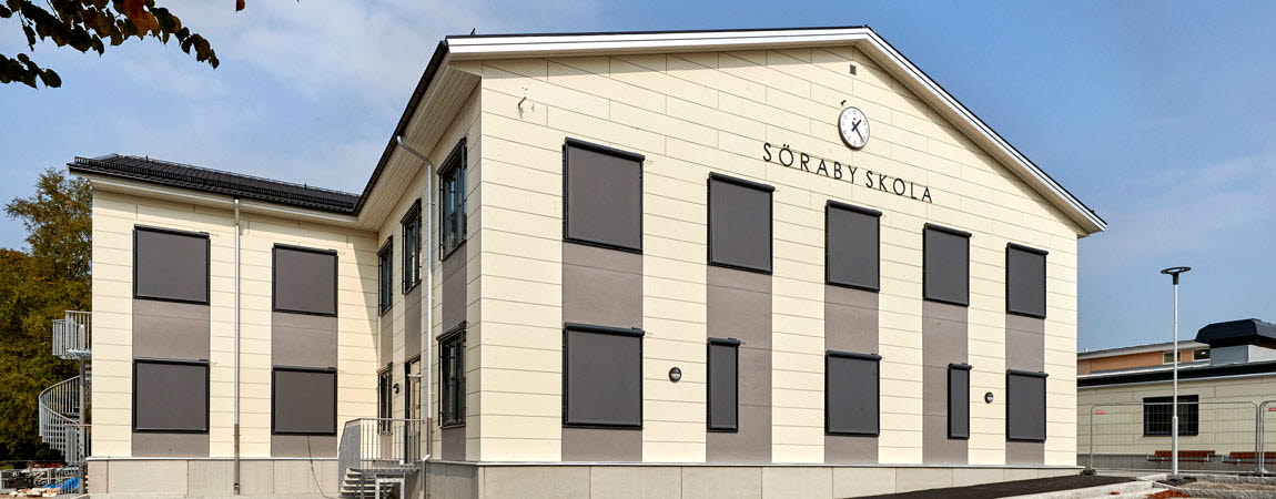 En vit byggnad, på fasaden står det Söraby skola i svarta stora bokstäver